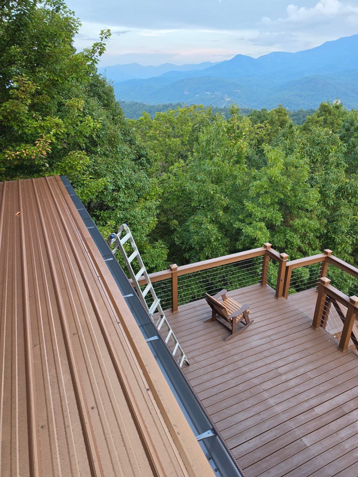 New gutter with leaf guard along a metal roof above a deck, with the Great Smoky Mountains behind, in Gatlinburg, Tennessee.
